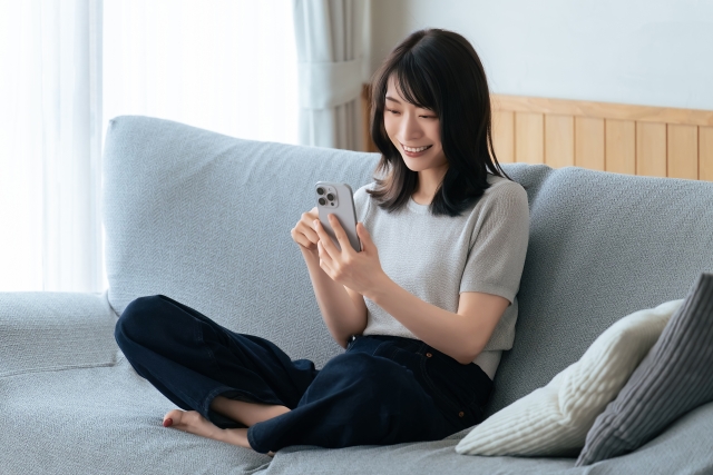 ソファーに座りスマホを見る女性